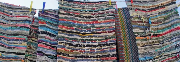 Fünf bunte Flickenteppiche hängen an einer Wäscheleine.